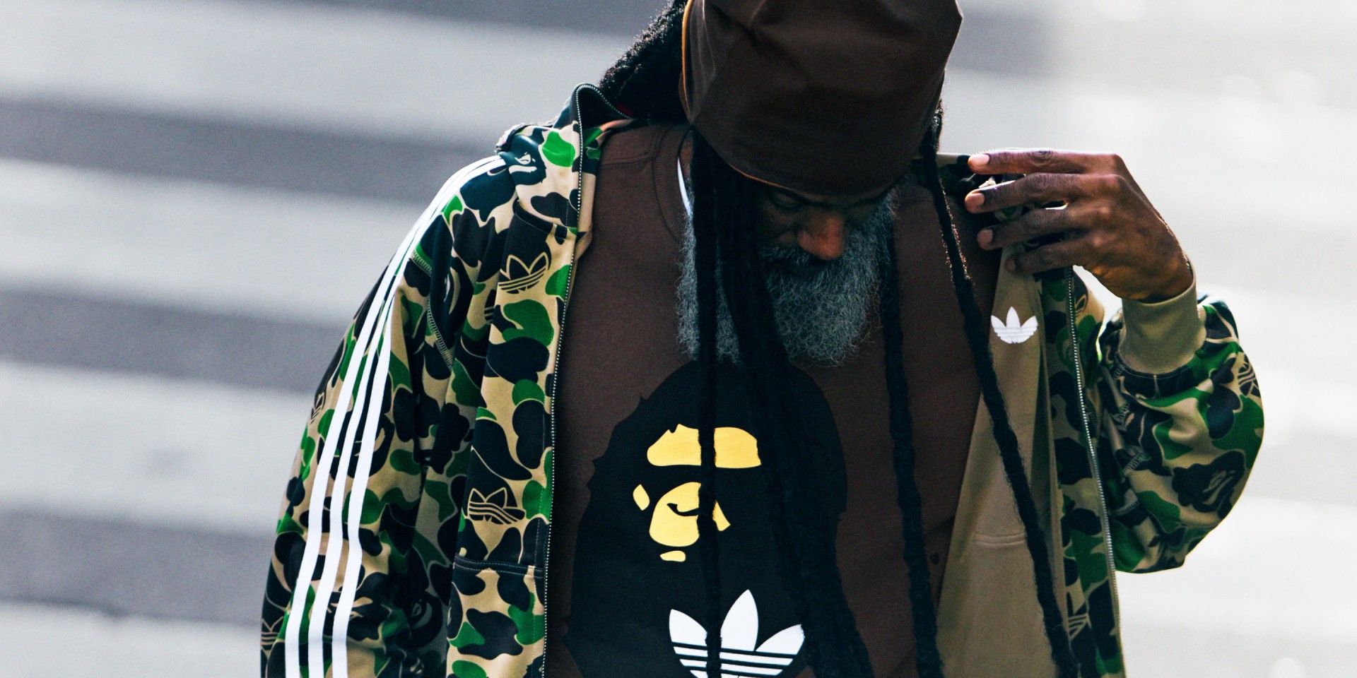 Iemand die een jack met camouflagepatroon draagt en het adidas logo zichtbaar heeft, en voor een vervaagde achtergrond staat.