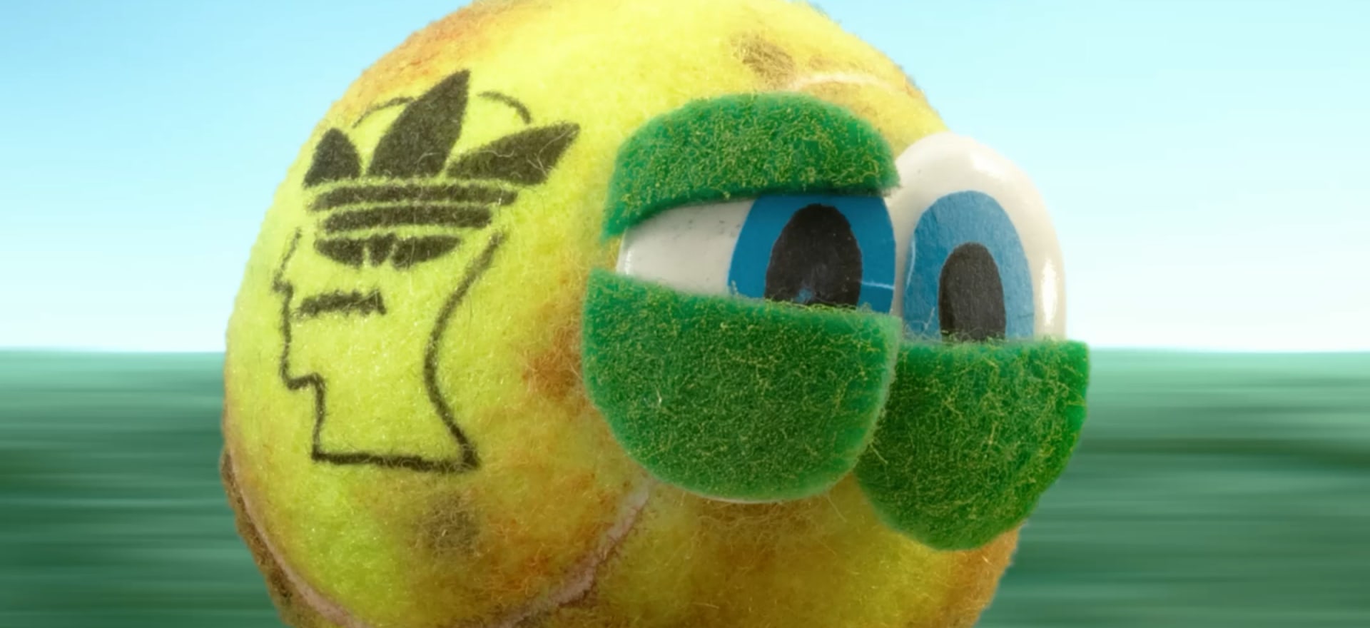 A yellow egg-shaped object with a grass-covered surface and Adidas logo, set against a blurred green background.