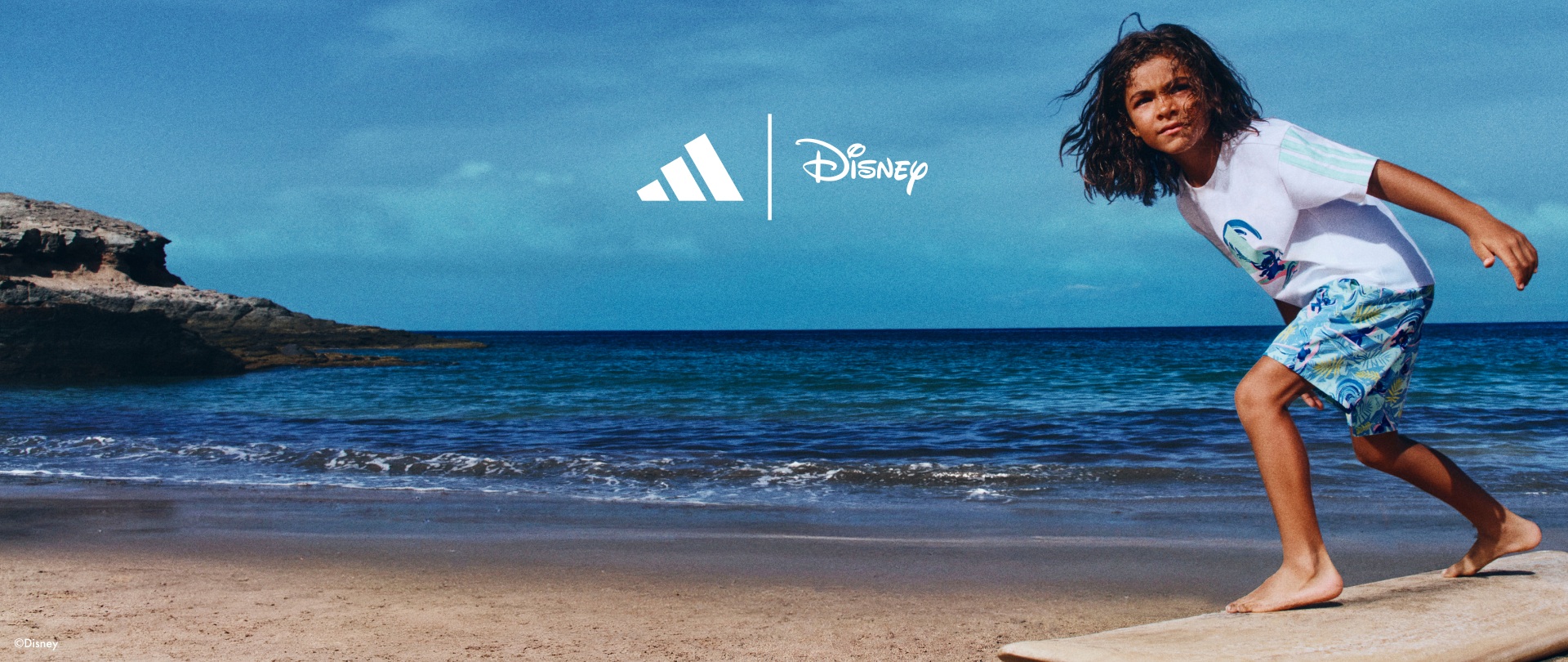 A young woman stands on a wooden platform on a beach, with a blue ocean and sky in the background, and the Adidas and Disney logos prominently displayed.