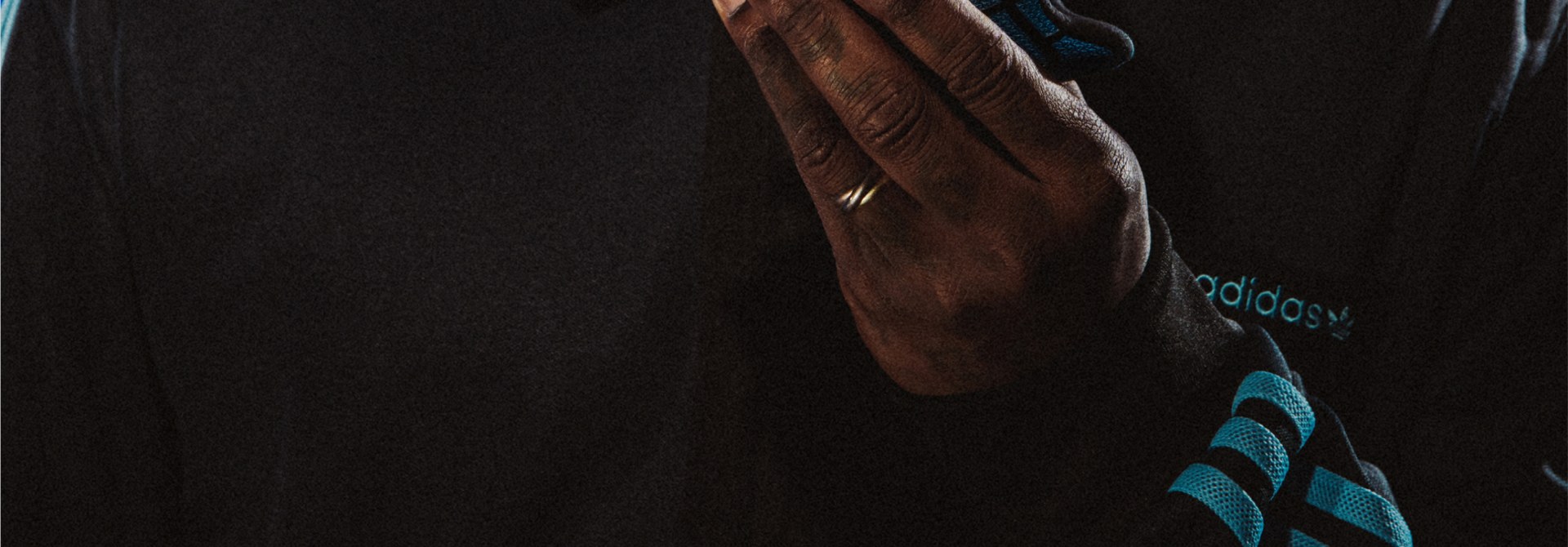 A close-up view of a person's hand wearing an Adidas sports glove against a dark background.