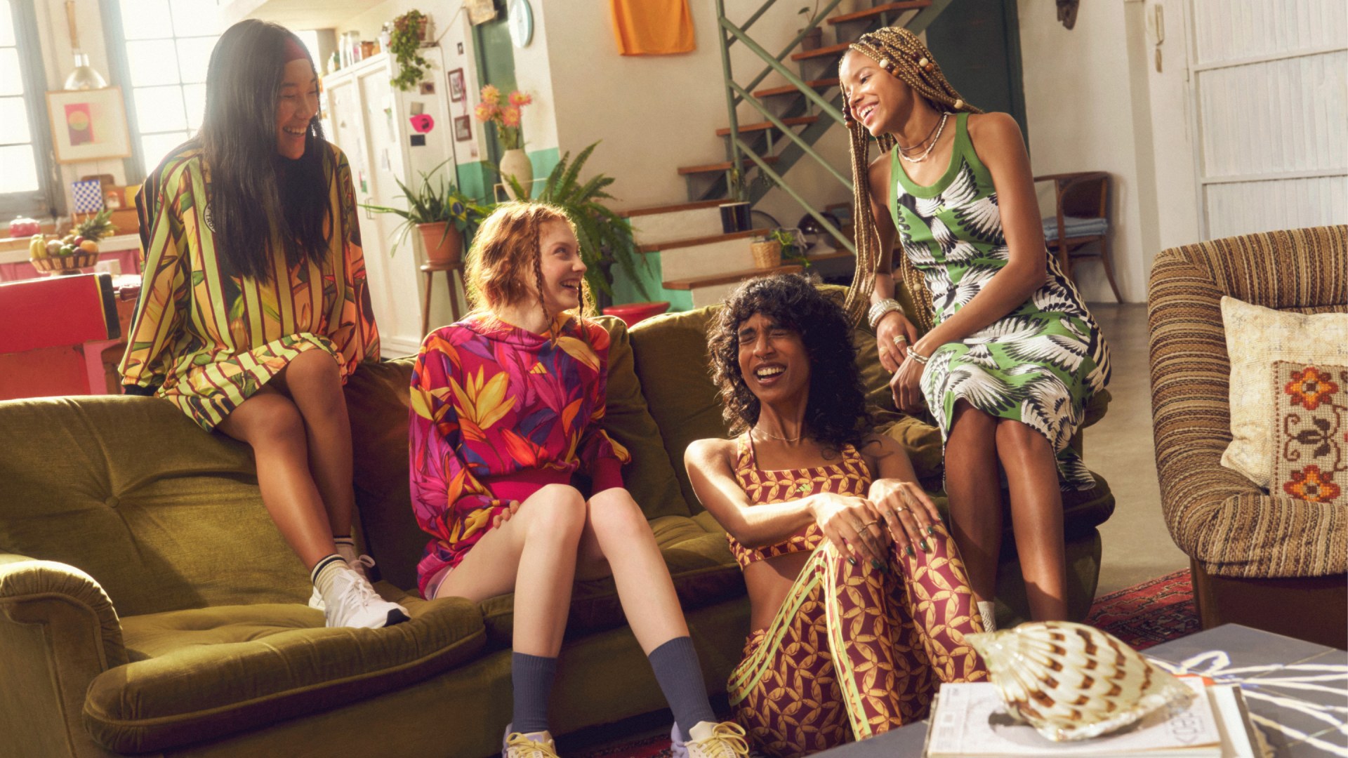 A group of young women, dressed in vibrant, patterned outfits, are gathered together in a cozy, eclectic living room setting, surrounded by various decorative elements and furnishings.
