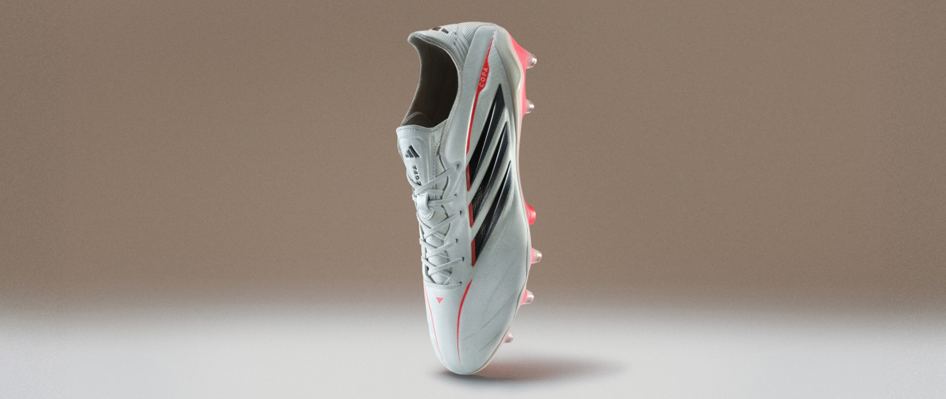 Esta imagen muestra una bota de fútbol de pie verticalmente en su puntera sobre un fondo marrón y blanco descolorido. 