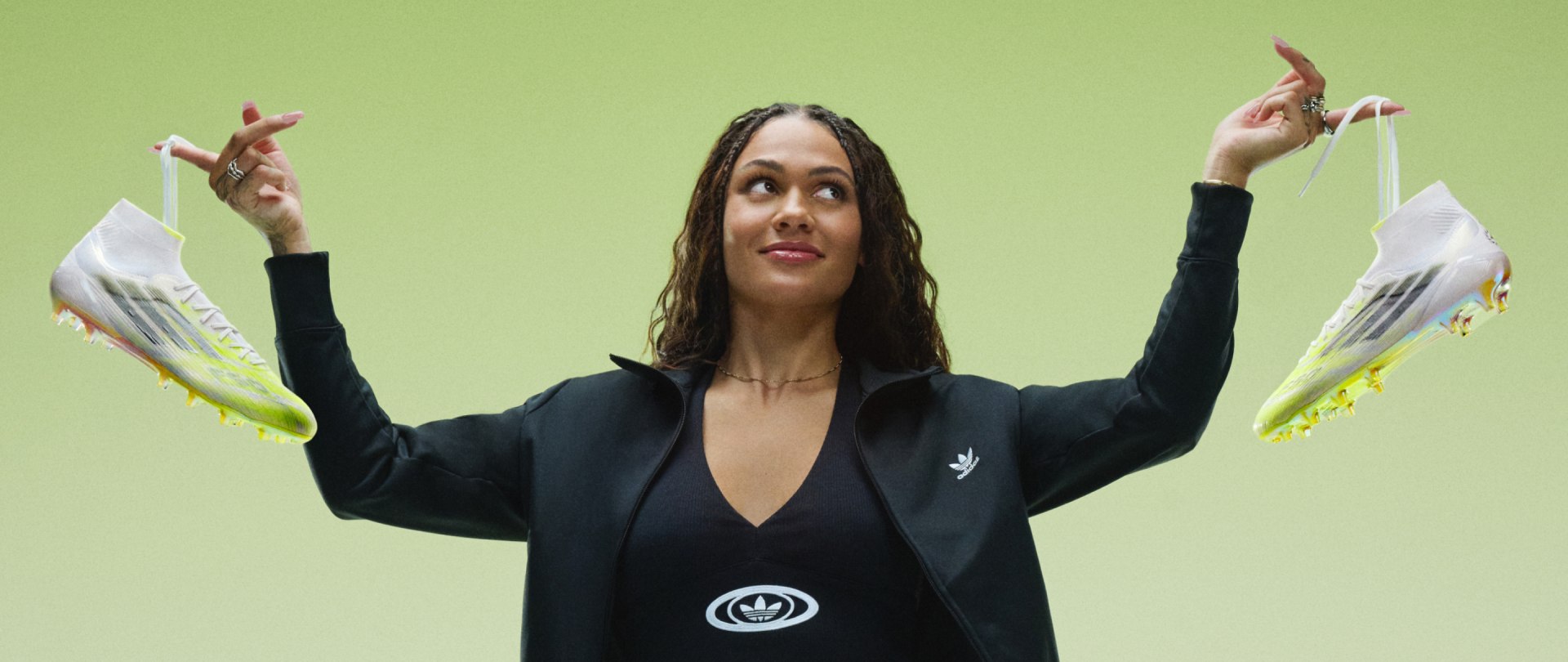This image depicts a woman holding a football boot in each hand by the laces against a faded lime green and white background.