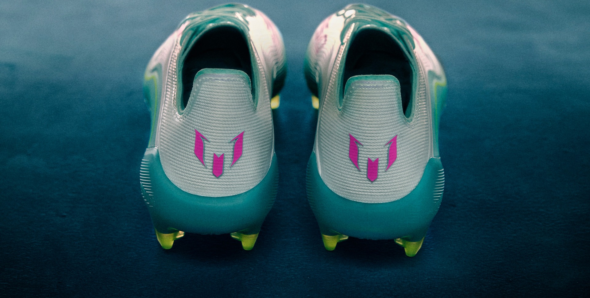 Back view of the adidas Messi F50 in white, blue, and red, photographed cleanly on a concrete floor.