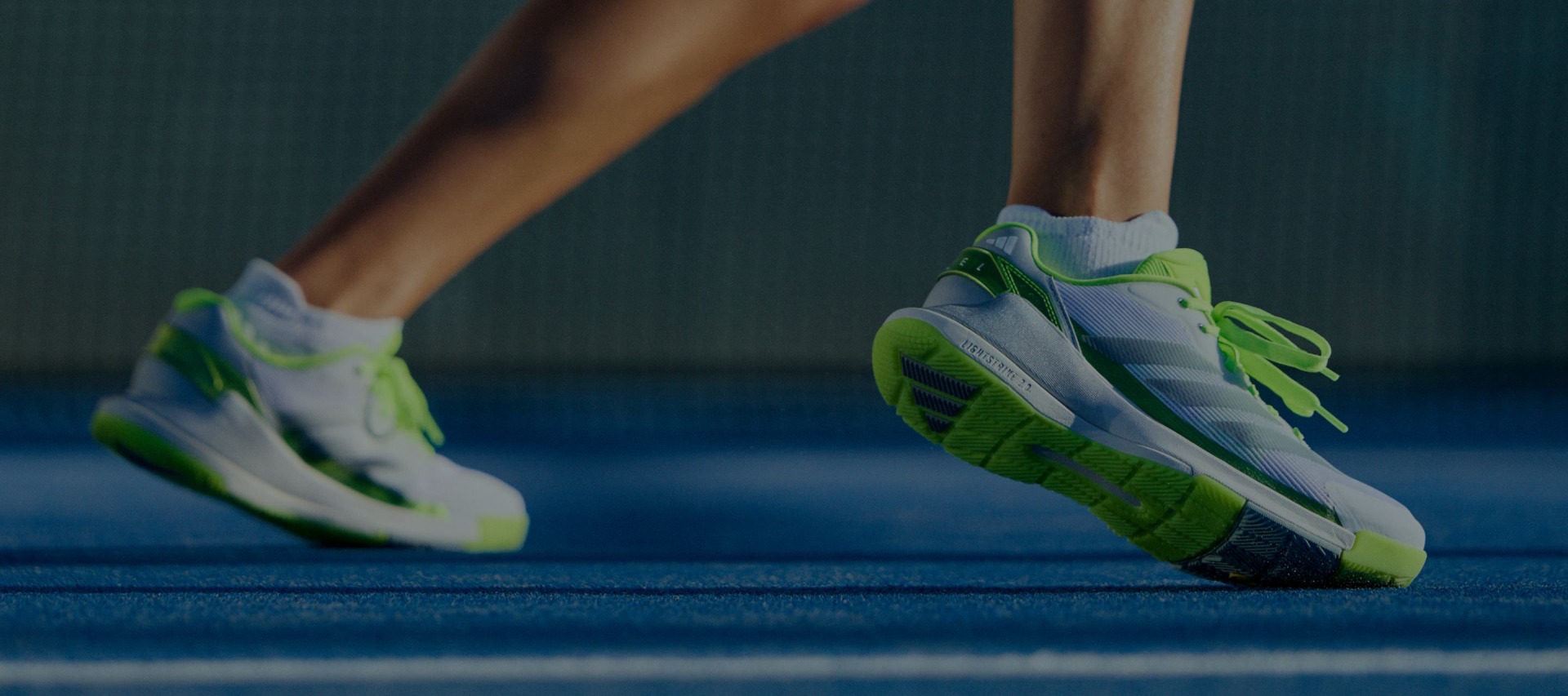 The image shows a pair of green and white athletic shoes on a blue padel court.