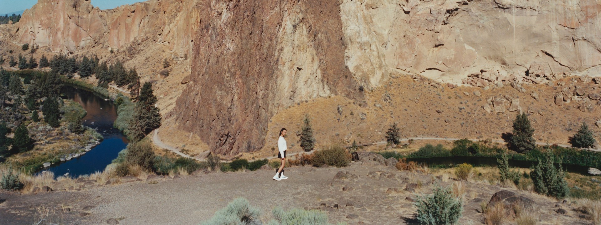 A rugged, rocky landscape with a winding dirt path leading through the foreground, surrounded by towering cliffs and a body of water in the background.