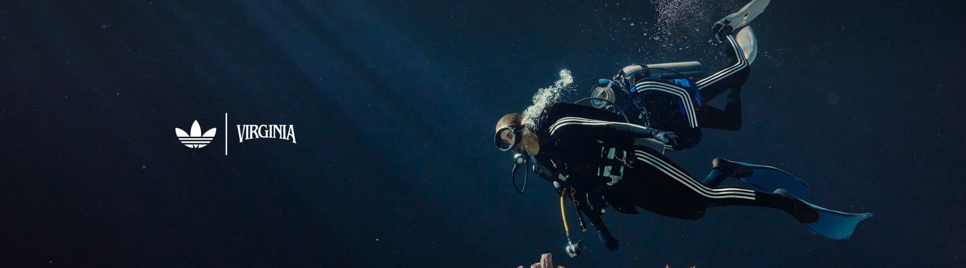 Un plongeur portant une combinaison noire avec des bandes adidas blanches nage près du corail coloré.