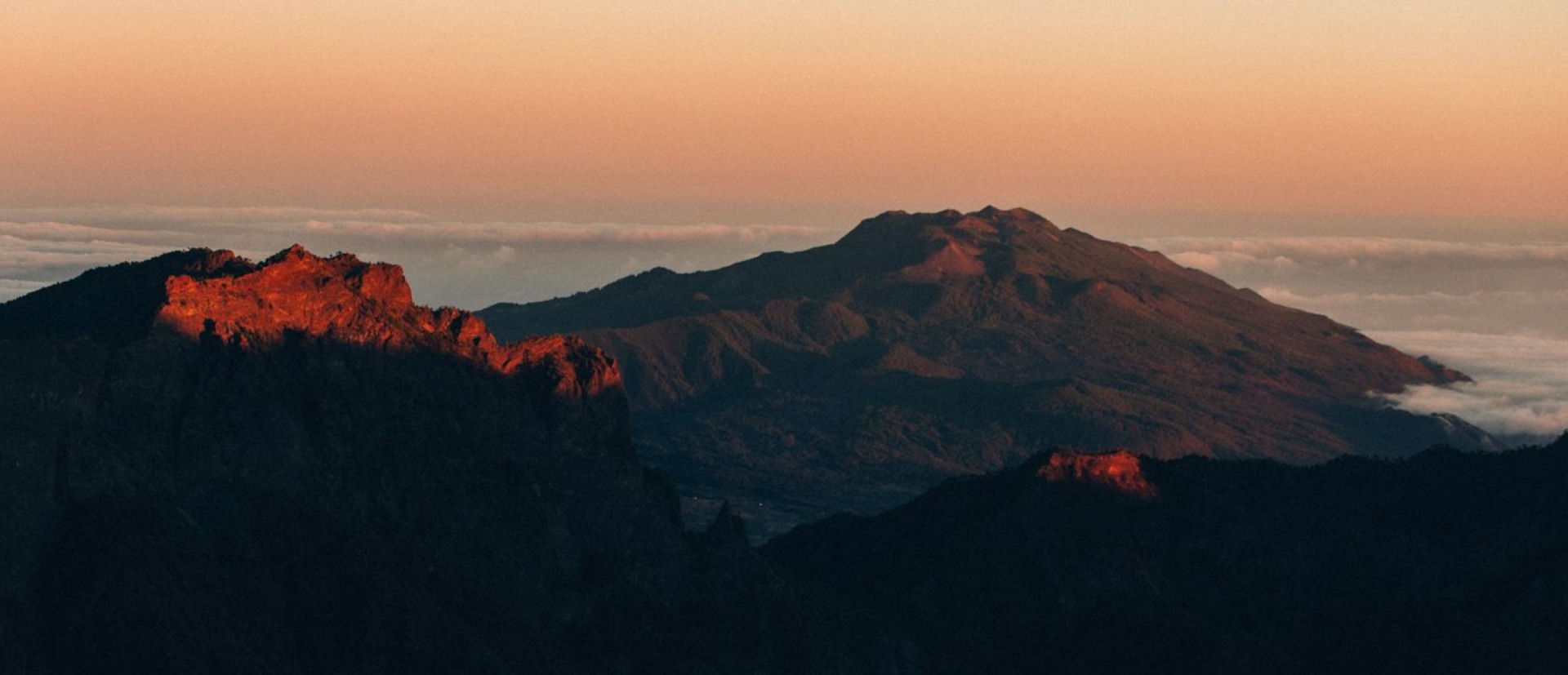 Coastal rocky landscape with mountains at sunset.