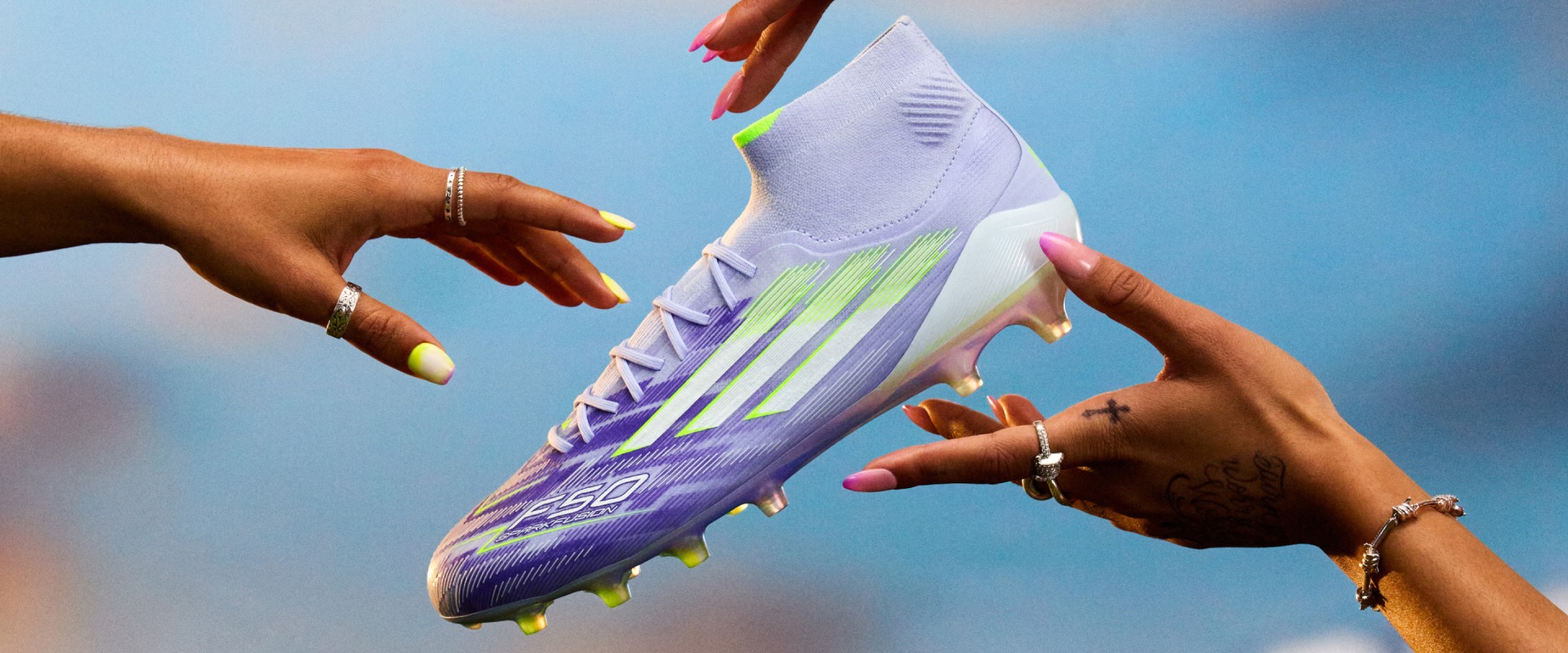 Hands reaching out to catch a purple and white F50 Sparkfusion soccer boot  against a bright blue sky.