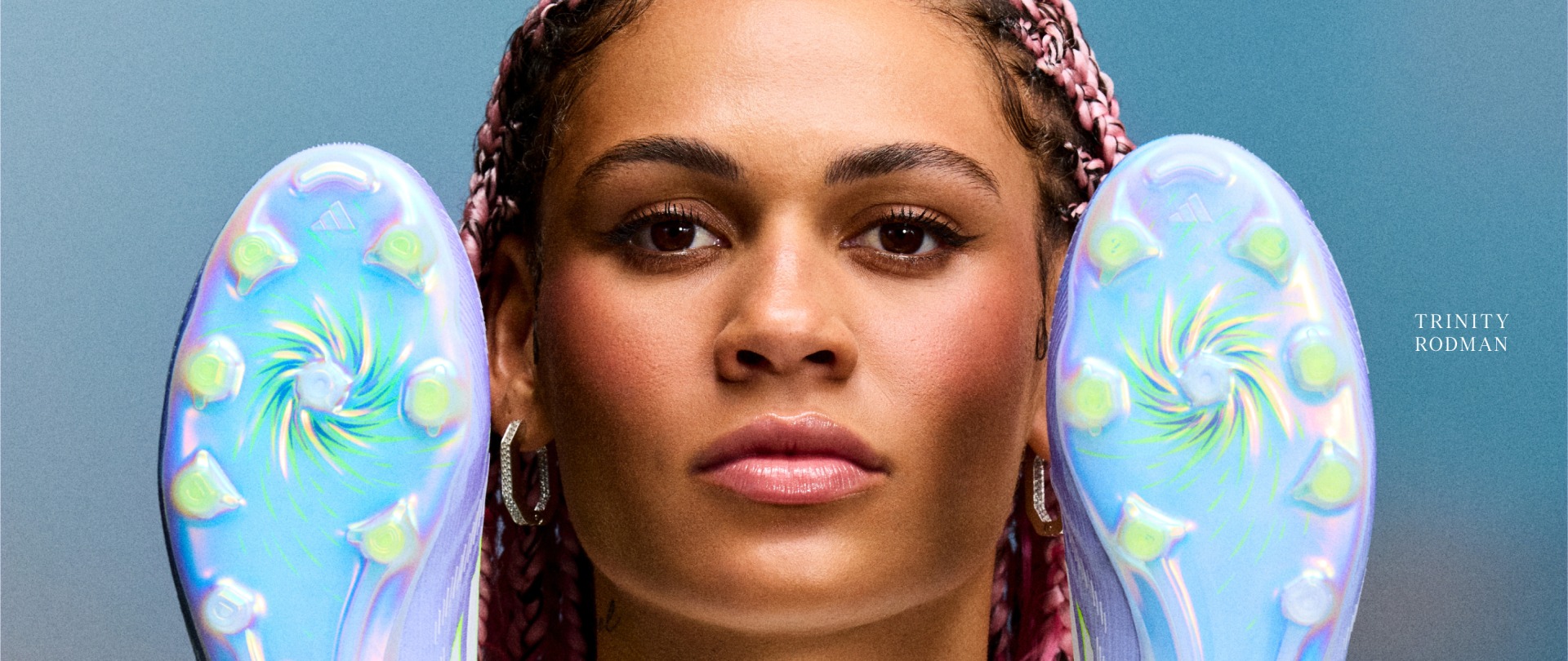 Trinity Rodman with colorful braided hair against a blue background, holding a pair of F50 Sparkfusion.