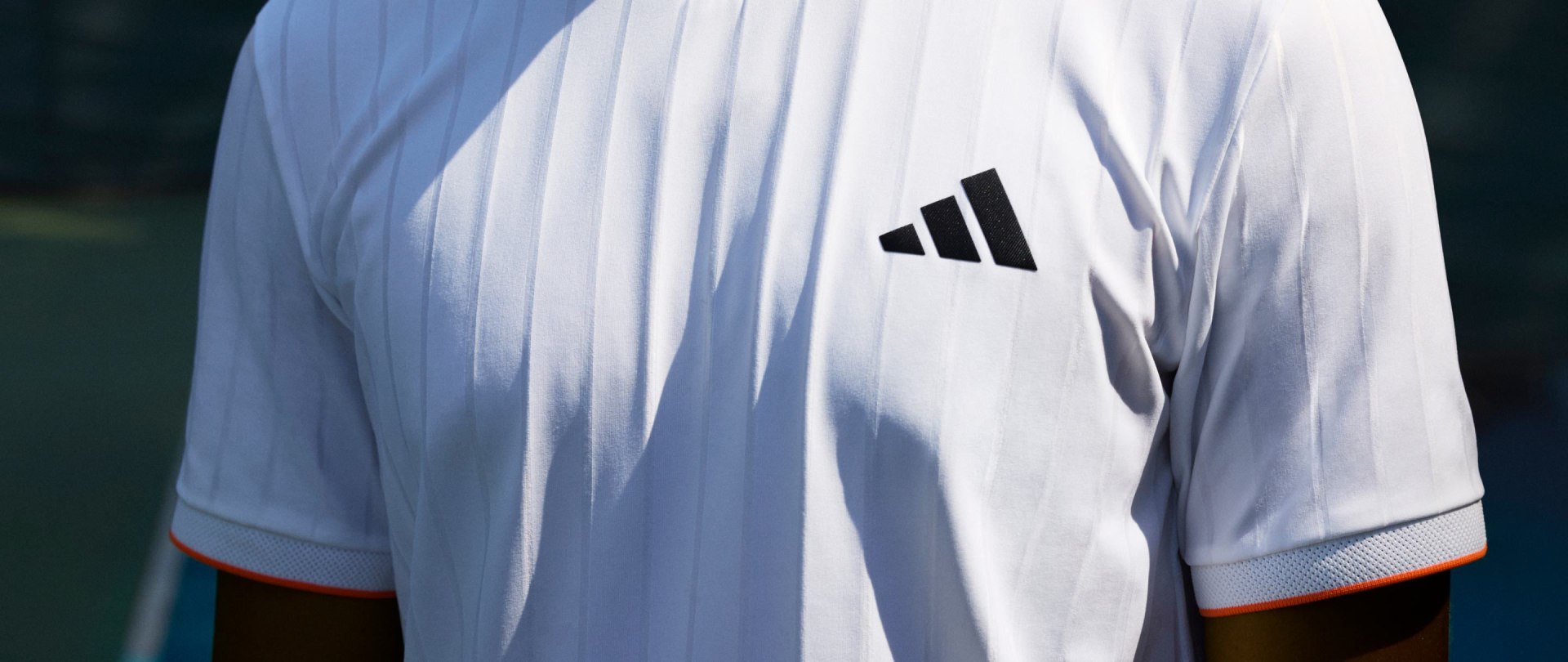 Una camiseta deportiva blanca con el logotipo de adidas sobre un fondo oscuro.