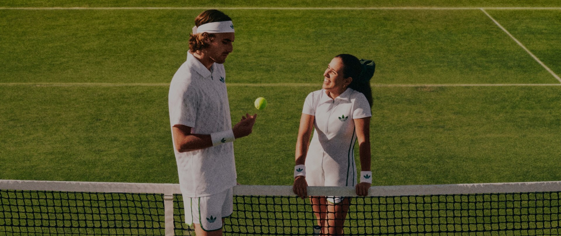 Tennis players Stefanos Tsitsipas and Camila Osorio chatting on a tennis court. They're both wearing the London Originals Collection.