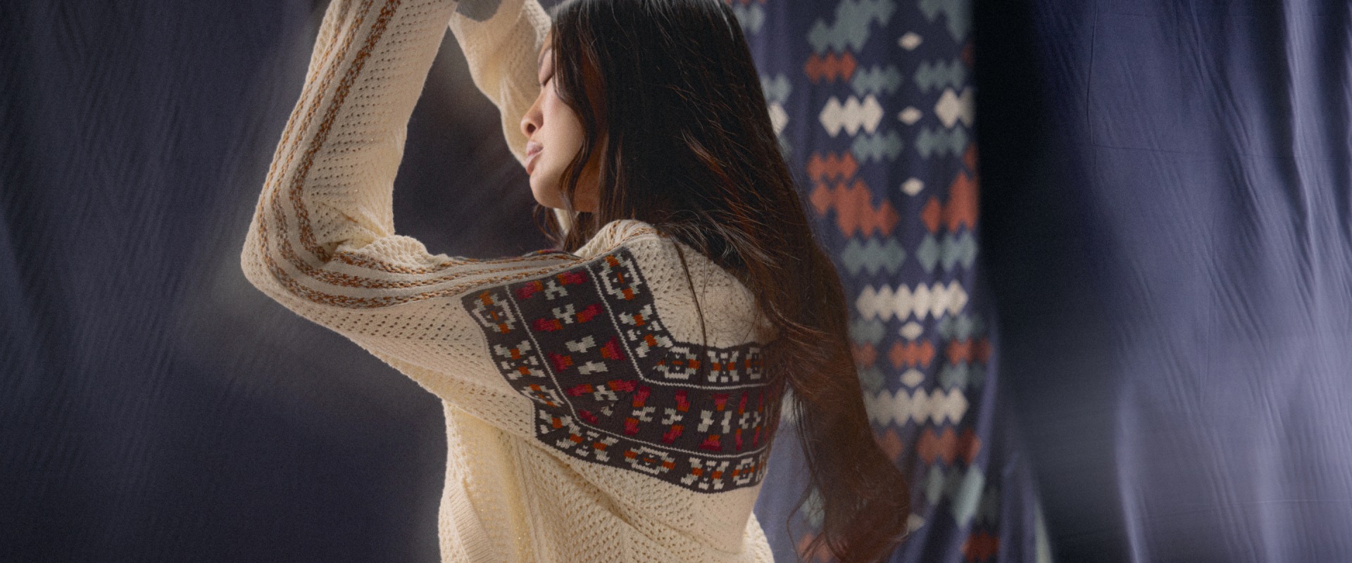 A woman dances in a cream crochet knitted adidas jacket with a geometric pattern and three beige adidas stripes along the sleeve.