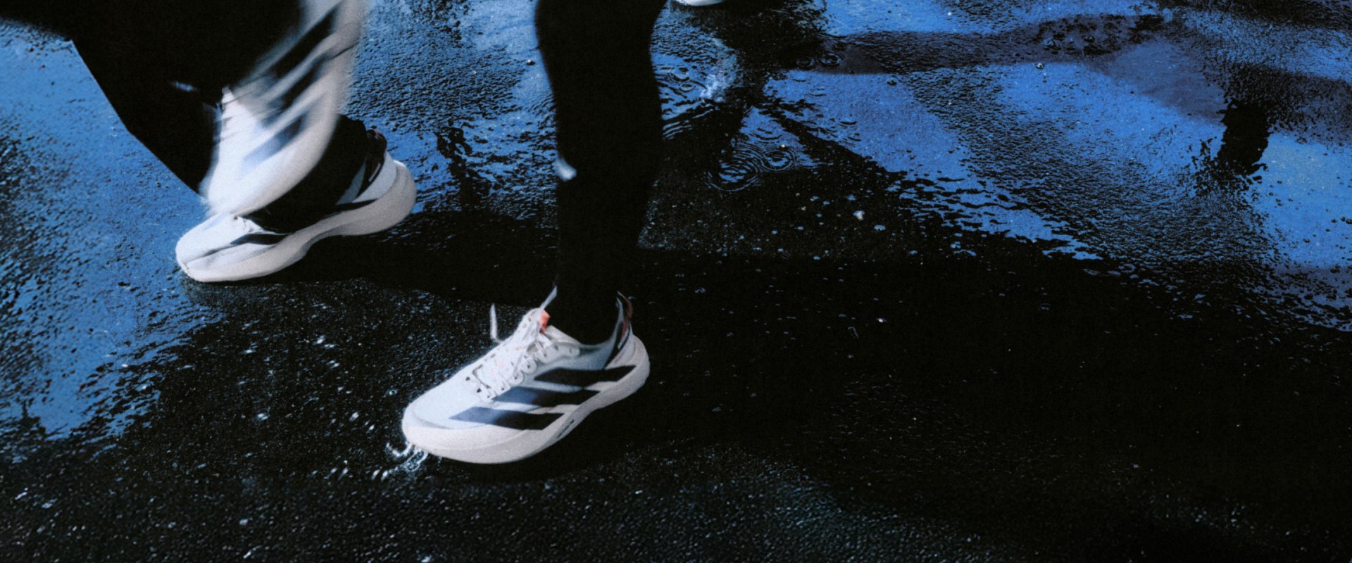 The image shows a pair of white sneakers standing on a wet, dark surface, with a blurred, blue-tinted background.