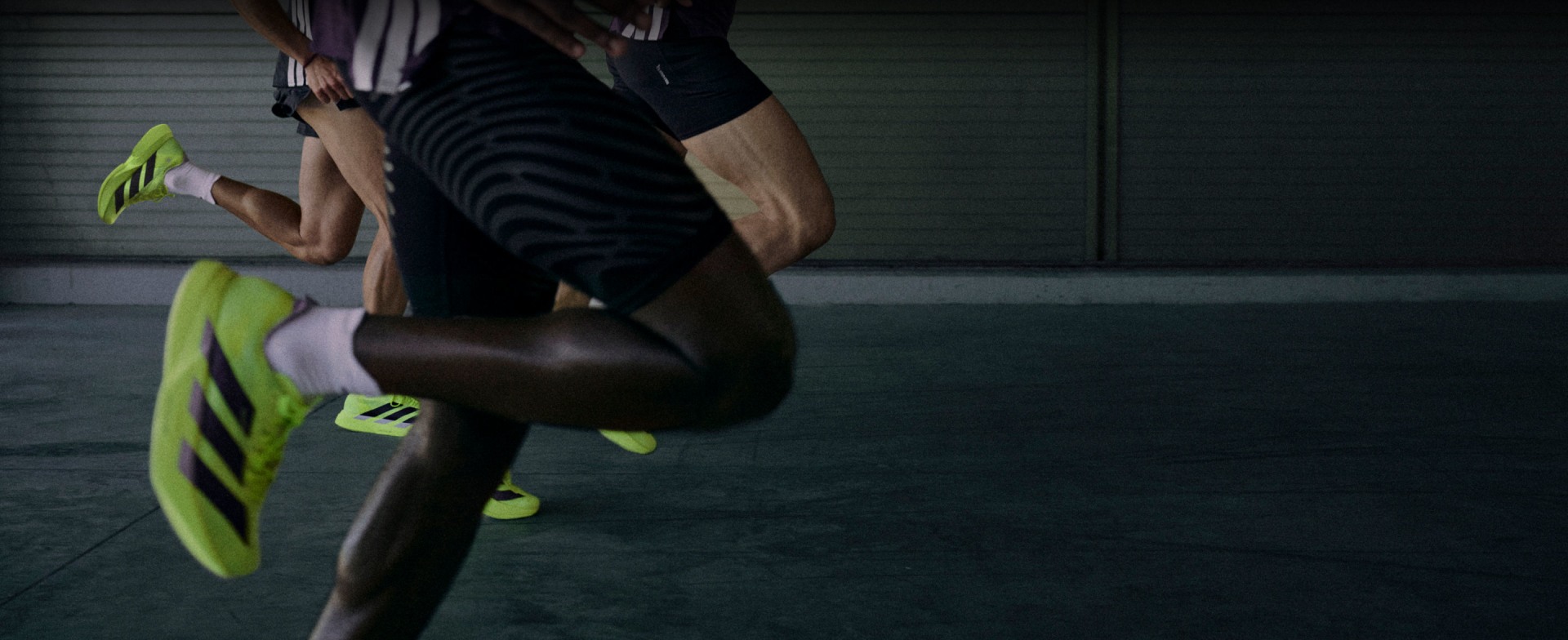 A person wearing a black and white striped shirt is holding a green surfboard in front of a green and gray background.