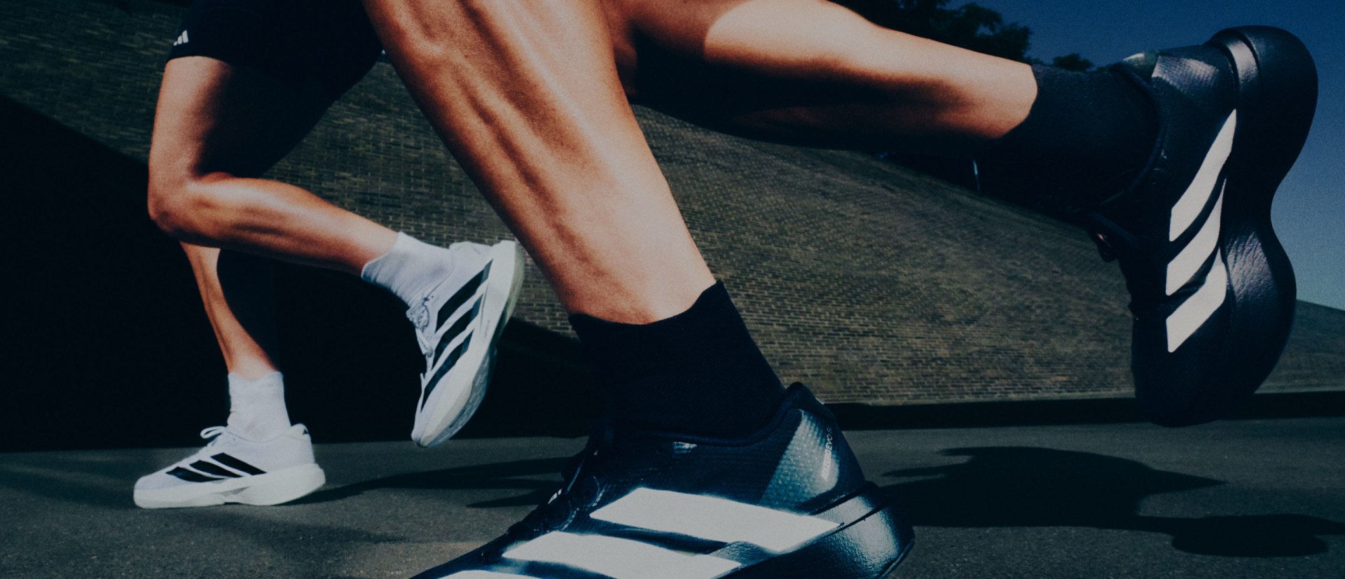 The image shows a person's lower body wearing athletic clothing, including black shorts and white sneakers, against a blurred background that appears to be a grassy or natural setting.