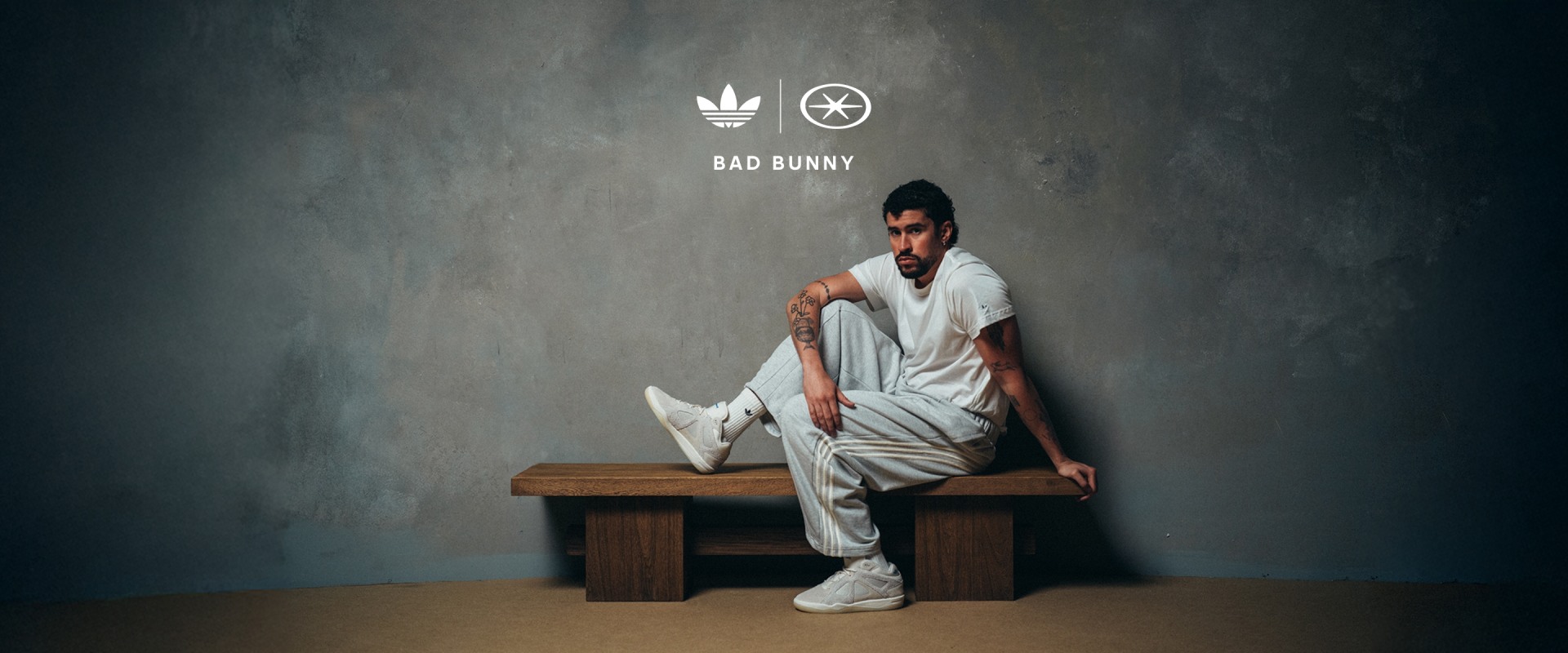 Black-and-white studio photograph of Bad Bunny crouching on a plinth, with shadow cast on the wall behind, creating a stark contrast between light and dark. A pair of sneakers sits on the floor.