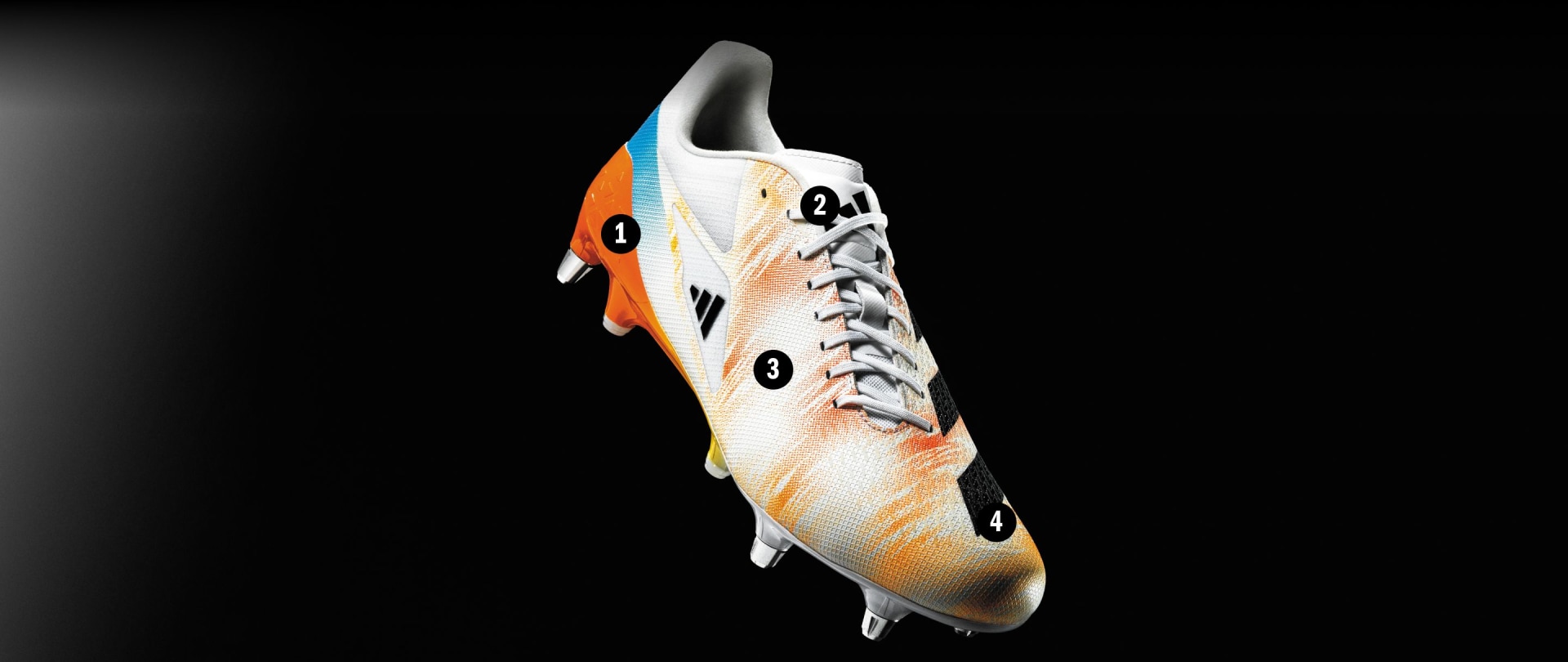 Λευκά και πορτοκαλί ποδοσφαιρικά παπούτσια με κορδόνια και τάπες σε μαύρο φόντο.