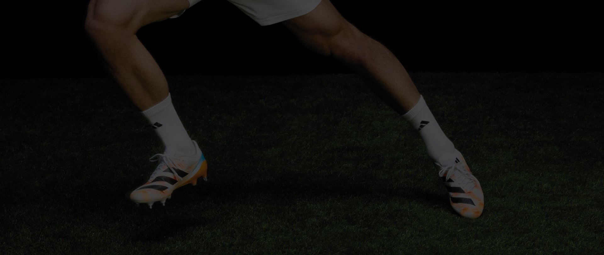 Η εικόνα δείχνει το κάτω μέρος του σώματος ενός ατόμου φορώντας σκούρα ρούχα και λευκά παπούτσια που στέκονται σε μια χλόη επιφάνεια σε ένα σκοτεινό περιβάλλον.