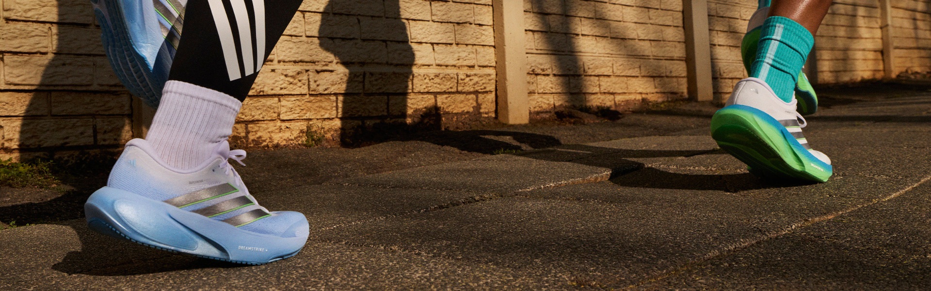 La imagen muestra un camino de hormigón que conduce a un muro de piedra, con sombras proyectadas por las estructuras circundantes que crean interesantes patrones en el suelo.