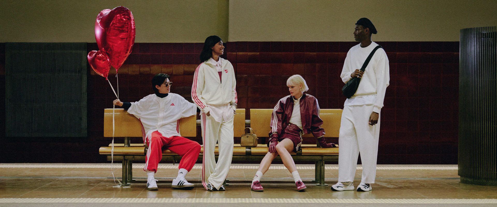 A group of individuals wearing stylish, coordinated outfits stand in a setting with a red heart-shaped balloon and a wooden bench in the background.