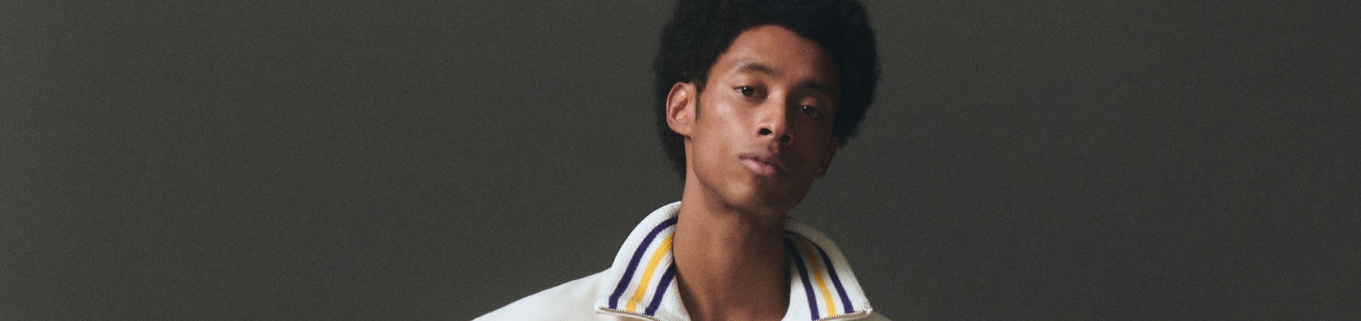A young man with a serious expression, wearing a white and striped shirt, against a dark background.