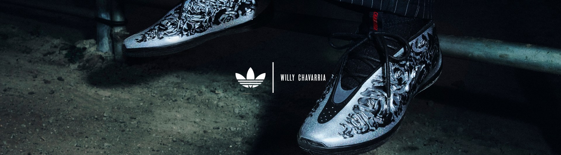Close-up of metallic silver adidas Originals x Willy Chavarria Harden V10 sneakers with embossed floral detailing, worn with black socks. The Trefoil logo and “WILLY CHAVARRIA” text appear centered in the image.
