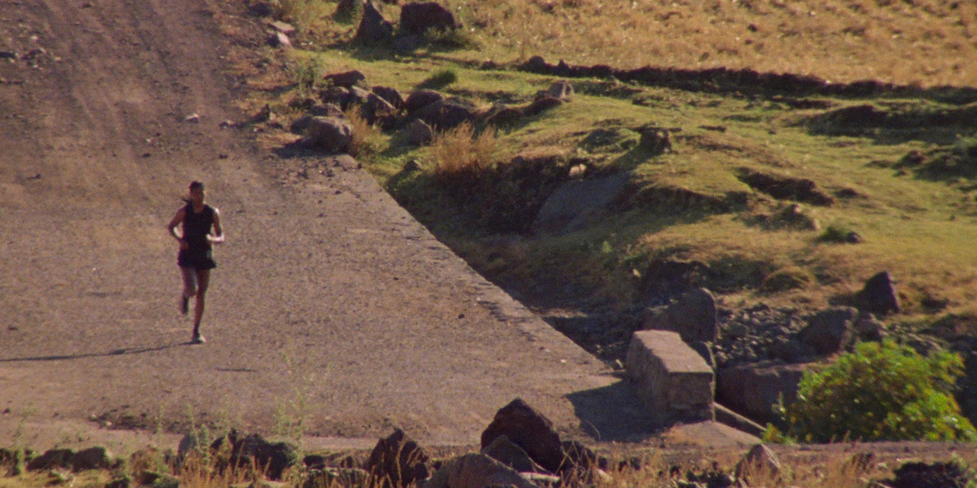 A zoomed out photograph captures Tigst Assefa as she runs through the Ethiopian Landscape.