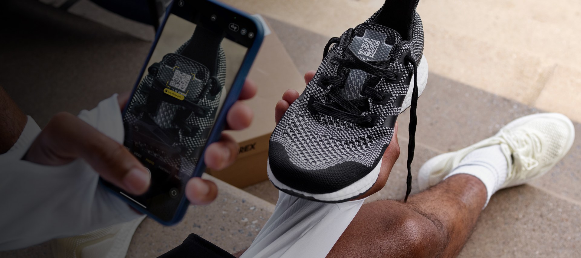 The image shows a close-up view of a pair of black and white sneakers, with a smartphone visible in the background.