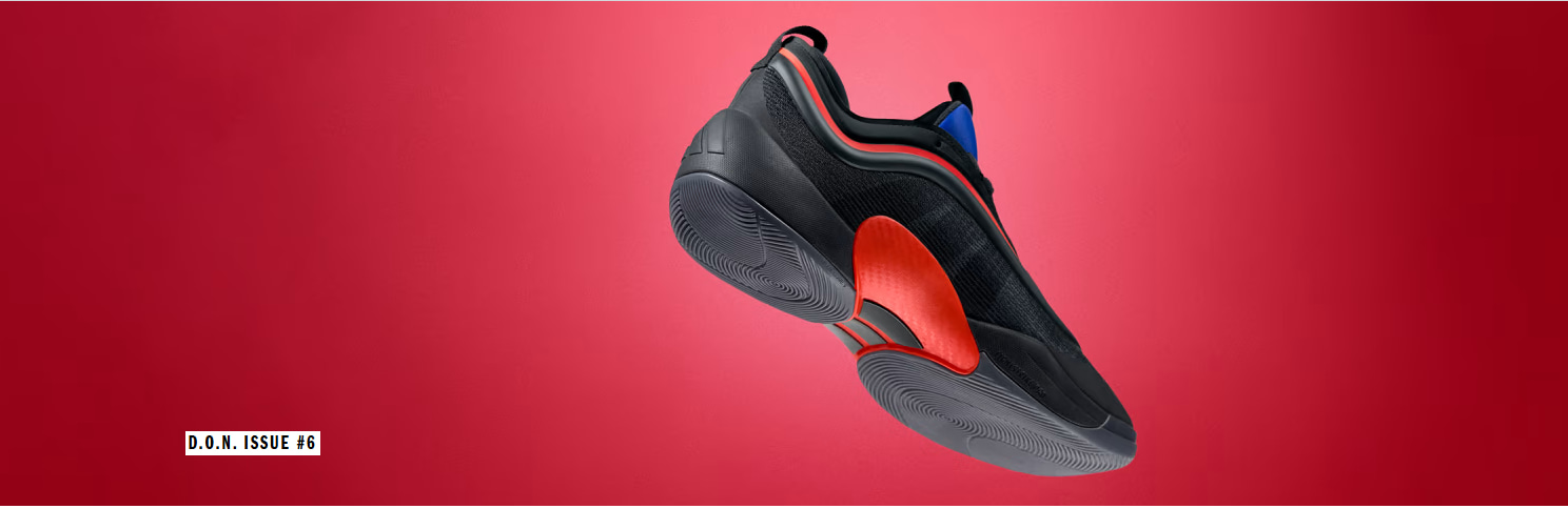 A sleek, futuristic-looking black and red shoe with a distinctive design and prominent sole stands against a vibrant red background.