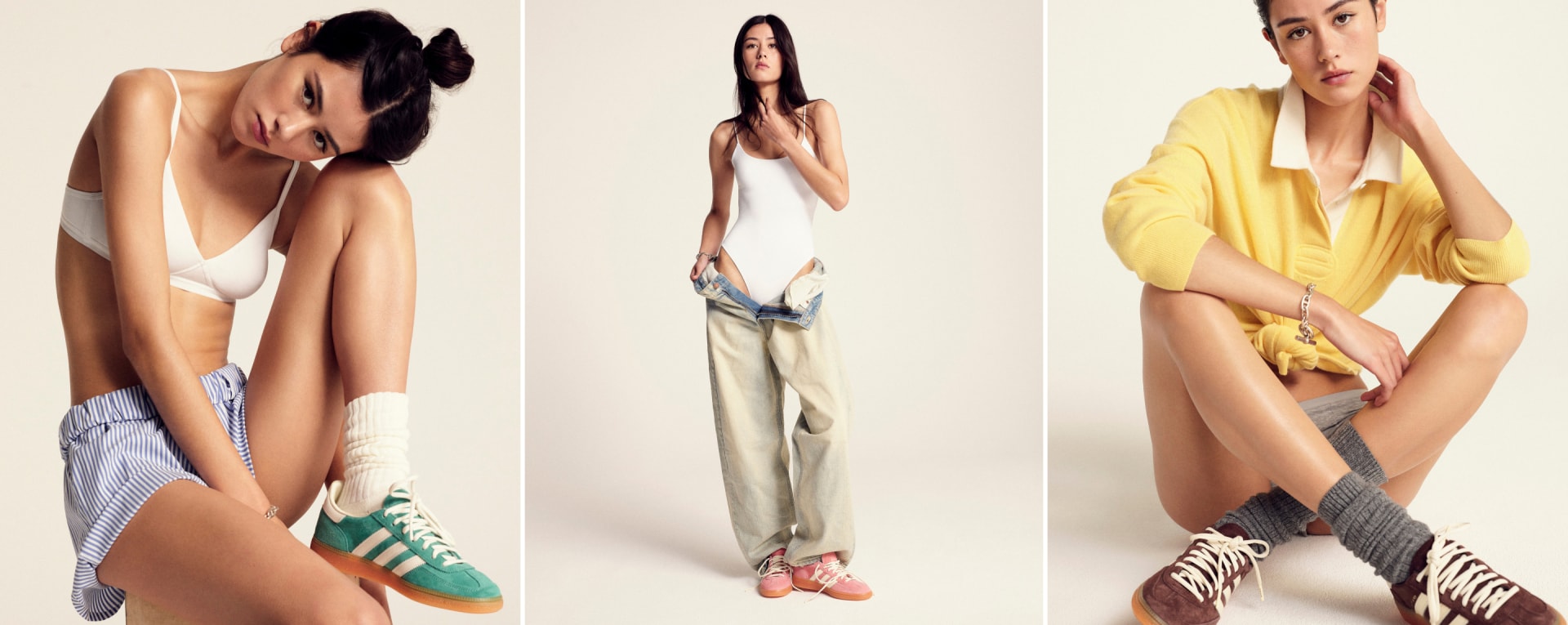 A brown-haired model strikes a pose against a white backdrop, sporting preppy attire paired with adidas Originals x Sporty & Rich shoes.