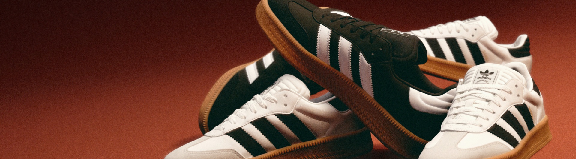 A pair of black and white Adidas sneakers with a gum sole, set against a reddish-brown background.
