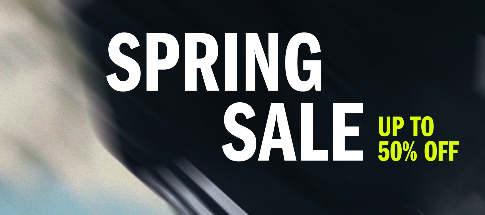 The image displays a large black and white sign advertising a "SPRING SALE" with a promotion of "UP TO 50% OFF" against a blurred background.