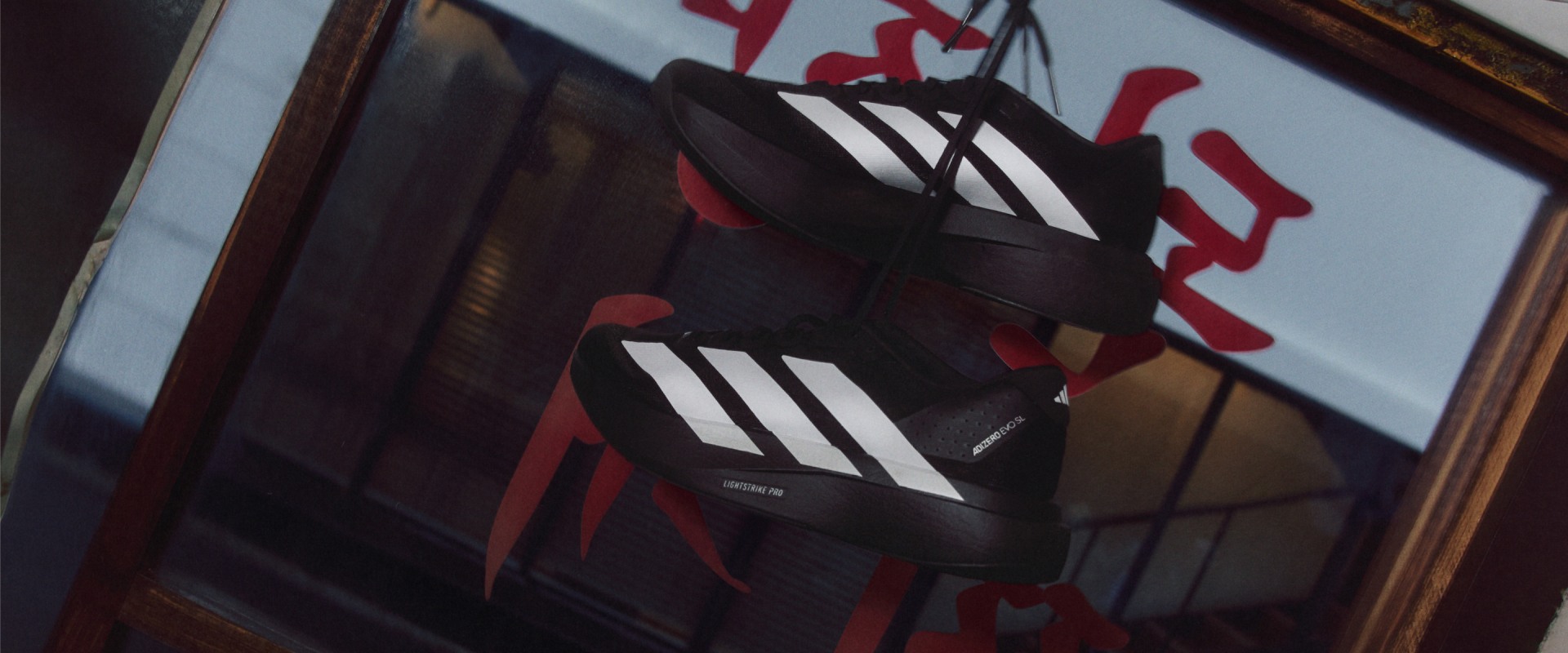 The image shows a pair of black and white athletic shoes with red accents, set against a blurred background of what appears to be a store display or shelving.