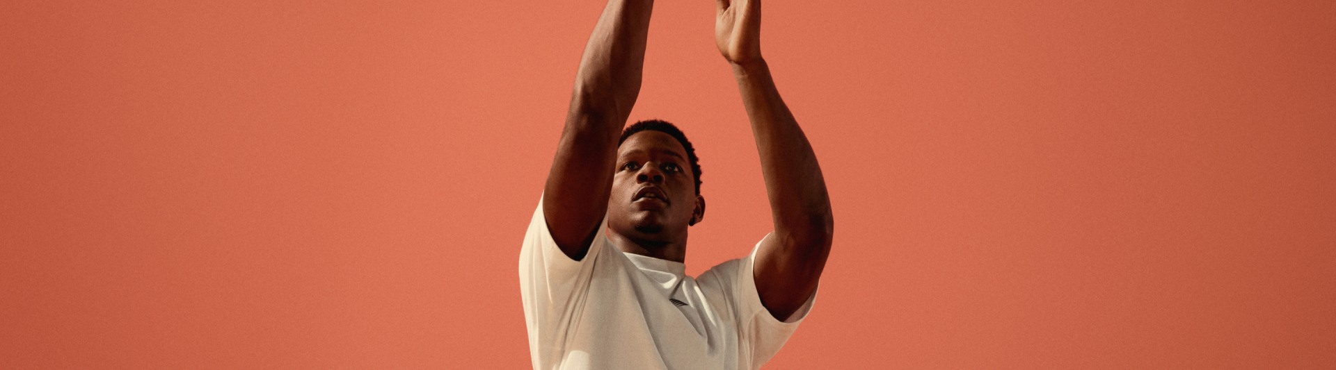 A person with their arms raised against a vibrant orange background.