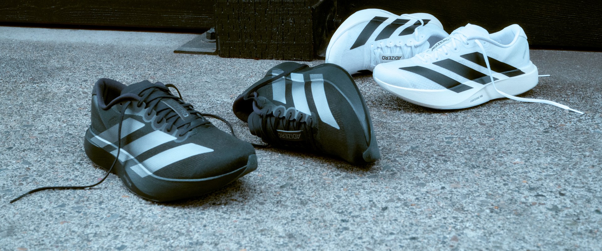 The image shows several pairs of Adidas athletic shoes, including black and white models, arranged on a tiled floor.