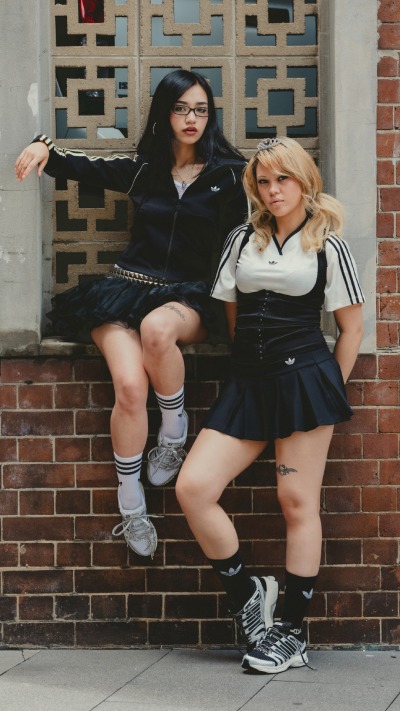Two young women in school uniforms sitting on a brick wall in front of a building.