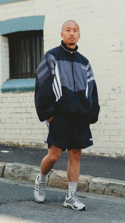 A person wearing a black and gray striped jacket stands in front of a brick building.