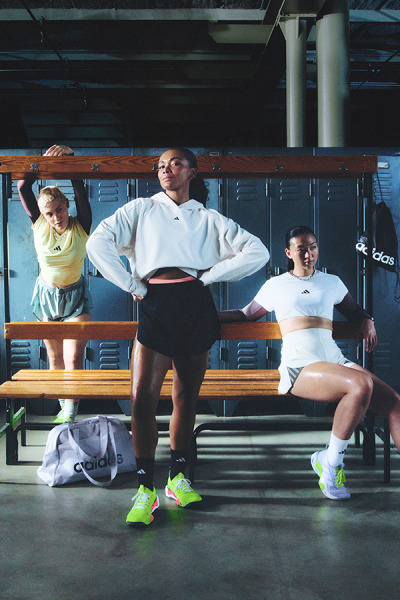 Three individuals, two women and one man, are seated on a bench in what appears to be a gym or fitness facility. The background features lockers and other equipment, suggesting a workout or training environment.