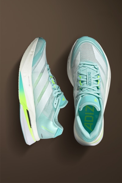 A pair of mint green and white athletic shoes with neon yellow accents, resting on a dark brown background.