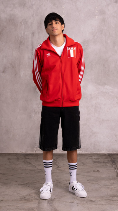 A young person wearing a red sports jacket with the Peruvian flag patch, standing in front of a plain gray background.