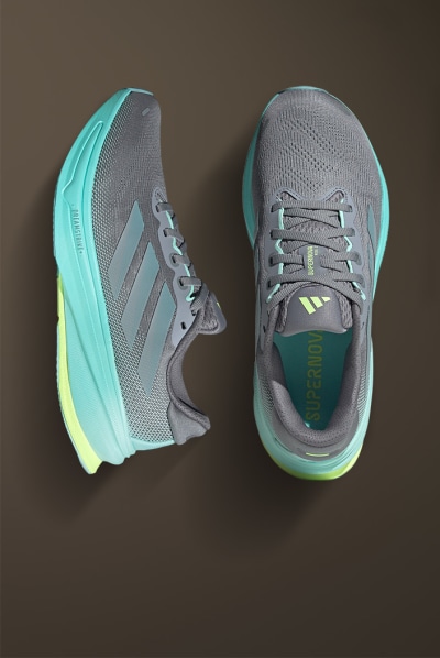 The image shows a pair of gray and mint green athletic shoes with yellow accents, resting on a dark brown surface.