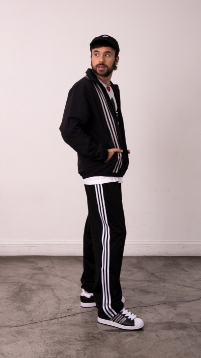 A person wearing a black tracksuit with white stripes, standing in a plain room with a concrete floor.