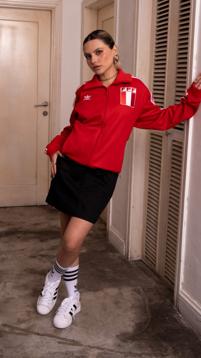 A person wearing a red sports jersey and black shorts stands in a room with a door and window visible in the background.