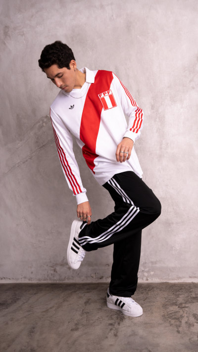A young person wearing a white and red athletic jacket and black pants is standing in a plain, gray-toned background, appearing to be in a dynamic pose.