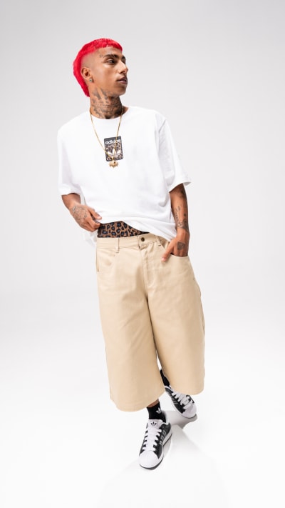 A person wearing a white t-shirt, red hat, and beige pants stands against a plain white background.