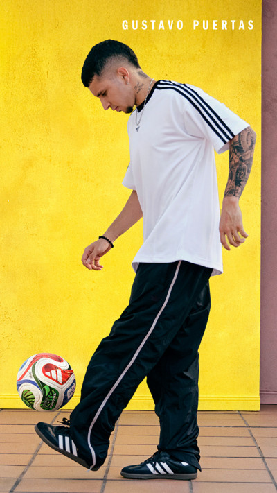 A young man in a white shirt and black pants is kicking a soccer ball on a yellow background.