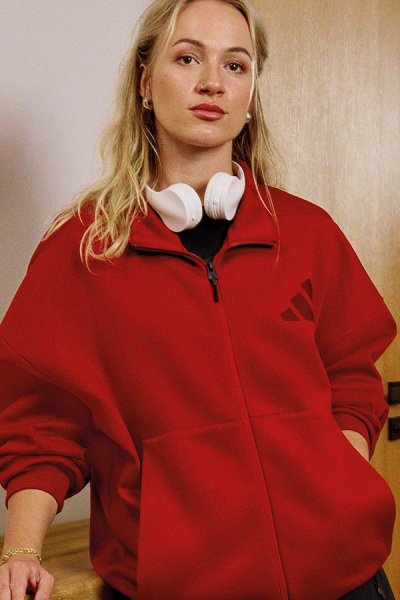 En ung kvinde med blondt hår iført en strålende rød jakke står foran en almindelig baggrund.