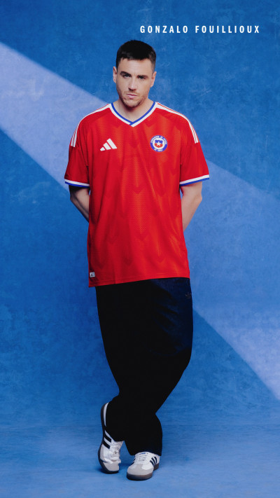 A man wearing a red sports jersey stands in front of a bright blue background.