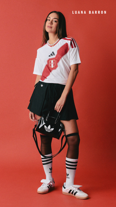 A young woman wearing a white sports jersey, black skirt, and white sneakers stands against a bright red background.